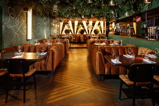 Bruine chesterfield banken en zwarte stoelen rond tafel in moderne restaurantruimte met groen wandpaneel en gouden verlichtin