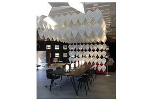 Moderne vergaderruimte met zwarte tafel, zwarte stoelen, witte bladvormige hangende akoestiekpanelen, wandkasten en rode zith