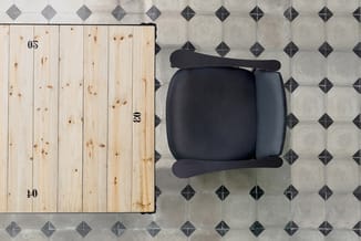 Zwarte bureaustoel met armsteunen gezien van bovenaf, geplaatst op tegelvloer naast houten oppervlak met nummers 05 en 40.