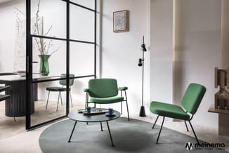 Loungeset met twee groene stoelen en ronde zwarte tafel op grijs tapijt, zwarte raamafscheiding, glazen vaas met takken, wand