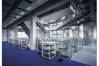 Modern kantoor met blauwe vloer, metalen trappenhuizen, glazen wanden en witte tafelgelegenheden met zwarte stoelen langs de