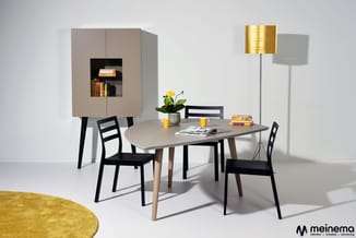 Moderne eetkamer met beige kastenwand, rond tafel met houten poten, zwarte stoelen, gele vloerlamp, potplant en geel tapijt.