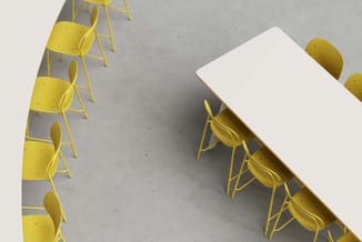 Gele stoelen rond een witte rechthoekige tafel in een kantoorruimte met betonnen vloer.