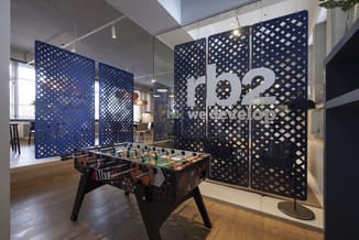 Kantoorruimte met blauwe akoestische wandpanelen, glazen wand met "rb2 welcoming" tekst, en tafelvoetbal in speelruimte.
