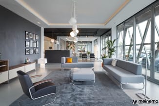 Modern kantoor met grijze zitbanken, zwart lederen fauteuil, pendant lampen, grote ramen, grijs vloerkleed en witmeubilair te