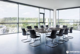 Moderne vergaderzaal met zwarte kantafel, zwarte kantorstoelen met chromen frames, grote raampartijen met groen uitzicht, don