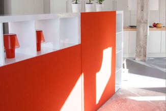 Moderne kantoorinrichting met rood gelakte scheidingswand en witte open kasten, rode tafellamp zichtbaar, betonnen kolom, dag
