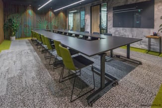 Moderne vergaderruimte met zwarte rechthoekige tafel, groene kantoorstoelen, houten accent wand, betonlook muren en gele vloe