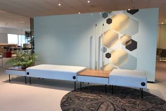 Blauwe modulaire bank met houten zittingsdeel en zwarte poten, tegen lichtblauwe wand met geometrische hexagon-details en gel