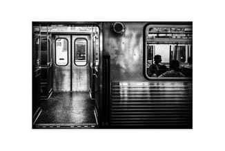 Zwart-witfoto van metrotrein interieur met dubbele deuren links en passagier zichtbaar achter raam rechts.