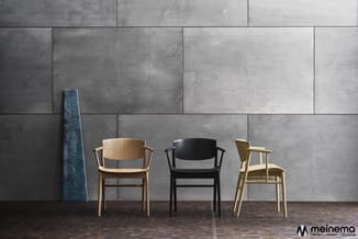 Drie houten stoelen met armleuningen tegen betonnen wand in verschillende houtsoorten: naturel, zwart en geel, op donkere vlo