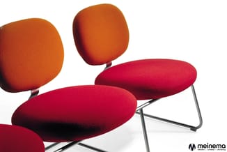 Moderne loungemeubels in rood en oranje met afgeronde vormen, metalen onderstel, tegen witte achtergrond. Meinema-logo zichtb