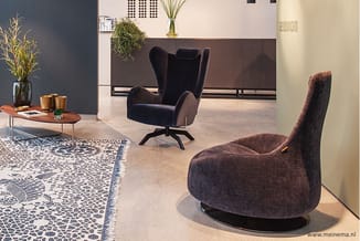 Showroom met twee paarse fluwelen fauteuils, houten bijzettafel met vaas, decoratief tapijt en bruine wandpanelen op betonvlo