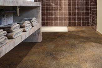 Moderne badkamer met bruine tegelvloer, betonnen wastafelmeubel, gestapelde grijze handdoeken en gemarmerde wandtegels.
