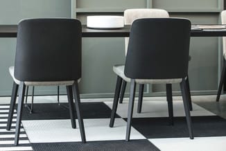 Twee zwarte stoelen met grijze zitgedeelten en donkere poten aan een tafel in een moderne kantoorruimte met grijs-witte wanda