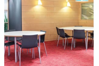 Kantoorruimte met twee ronde vergadertafels, zwarte stoelen, rode tapijt, houten wandbekleding en spotlights.
