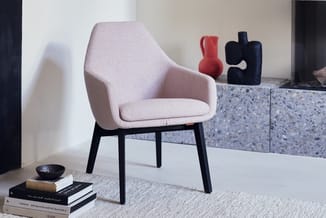 Roze stoffen loungestoel met zwarte poten in moderne kantooromgeving, naast boeken en decoratieve objecten.