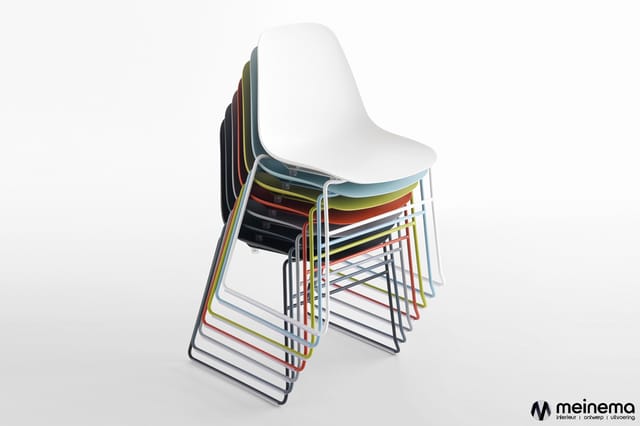 Gestapelde kunststof stoelen met metalen buisframe in verschillende kleuren (wit, zwart, rood, geel, grijs) tegen witte achte
