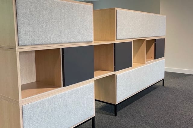 Modulaire kasten in kantoor met houten frame, grijze stofpanelen en donkerblauwe deuren, gerangschikt in twee rijen.