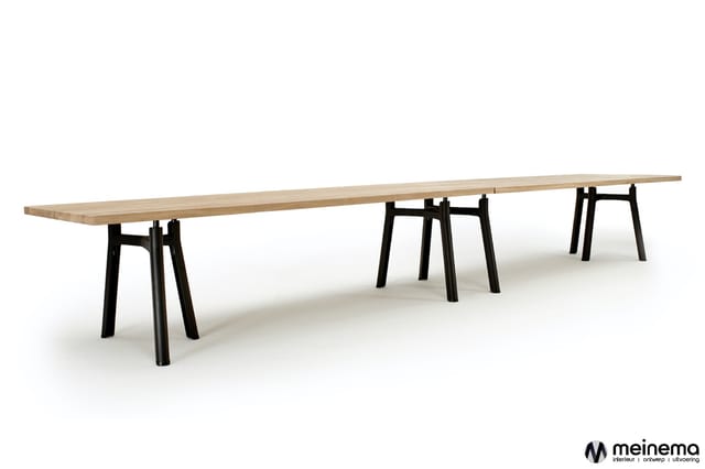 Lange houten vergadertafel met natuurlijke afwerking op drie zwarte trapeziumvormige onderstellen, tegen witte achtergrond.