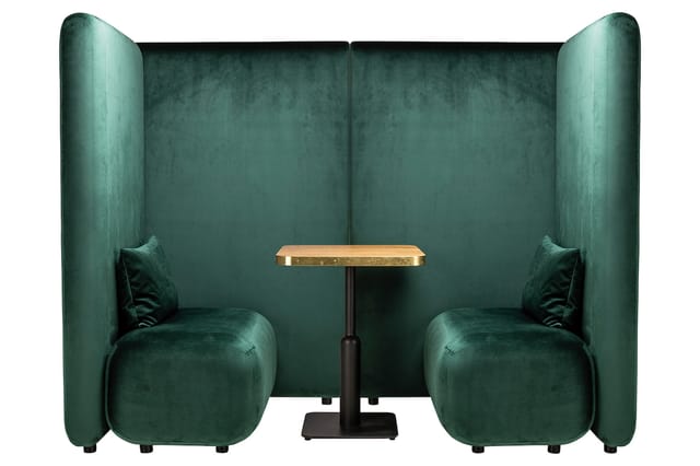 Groen fluwelen belcel met twee stoelen, houten tafel en hoge wanden voor akoestische privacy.
