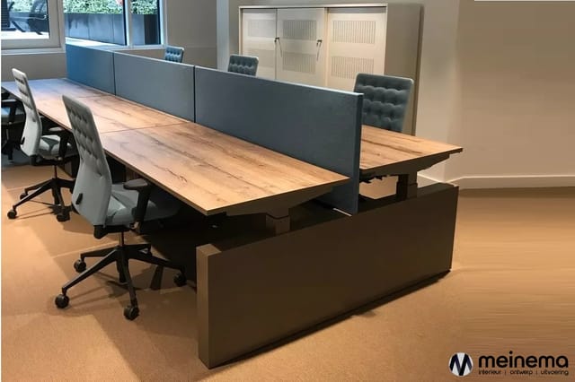 Lange werkplek met houten blad en grijze akoestische scheidingswanden, inclusief bureaustoelen en opbergkast.