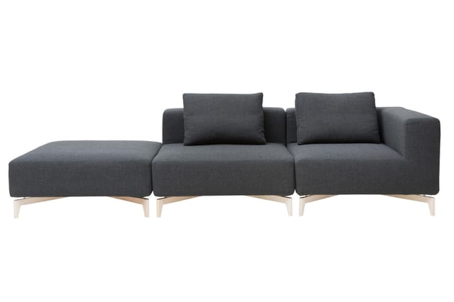 Grijze modulaire bank met chaise longue links, twee zitplaatsen met rugkussens en natuurhouten poten op witte achtergrond.