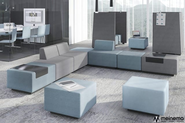 Modern kantoorinterieur met modulaire blauwe en grijze zitmodules, losse poefs, werkplek met schermen en grote ramen met uitz