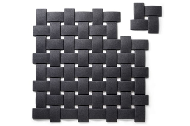 Grijze akoestische wandpanelen in vlechtpatroon met 3D-effect, enkele panelen losgekoppeld rechtsboven.