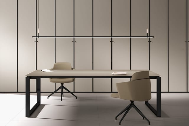 Moderne kantoorruimte met zwart bureau, beige draaistoelen en hangende verlichting tegen grijze paneelwand.