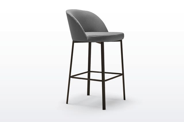 Grijze barstoel met gewelfde rugleuning, zitting en voetsteun, op zwart metalen frame tegen witte achtergrond.