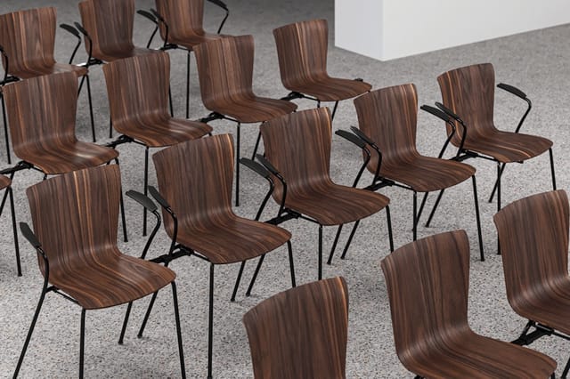 Bruine houten stoelen met zwarte metalen poten, losjes geplaatst op betonnen vloer in kantoorruimte.