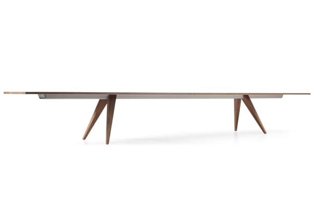 Lange houten vergadertafel met grijs blad en twee houten stellages met schuin geplaatste poten, zijaanzicht.