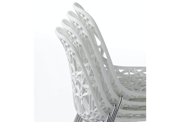 Witte moderne stoel met opengewerkt rugleuning en geometrisch patroon, zijprofiel op wit oppervlak.