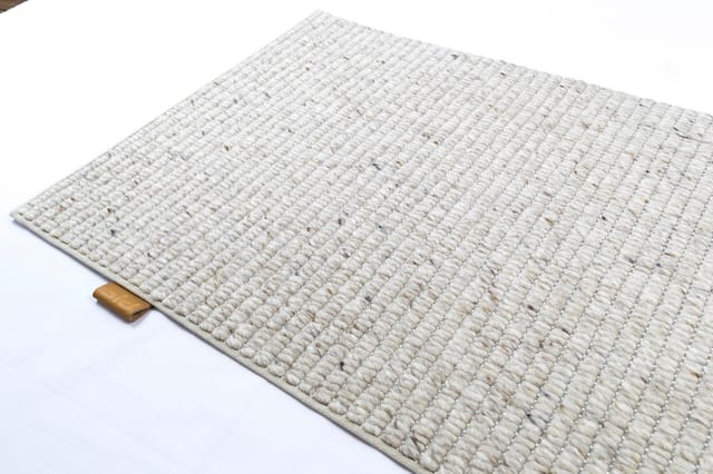 Crèmekleurig woven tapijt met ribbelpatroon en houten rand, schuin gefotografeerd op witte achtergrond.