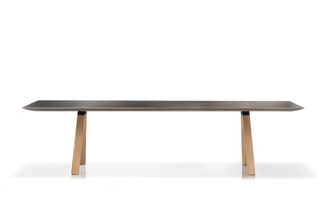 Lange vergadertafel met donkergrijs blad en houten poten in natuurlijke tint, frontale weergave tegen witte achtergrond.