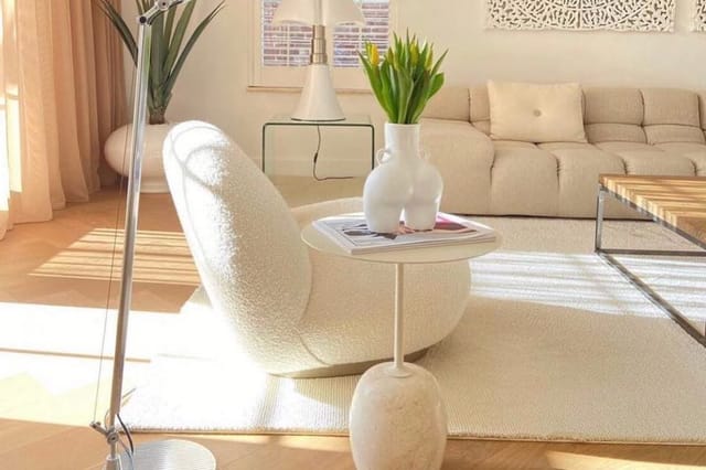 Moderne woonkamer met crème-kleurig fauteuil, bijzettafel, beige bank, houten vloer en ronde witte vazen met groen.