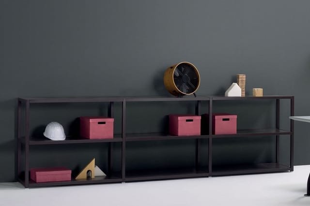 Donkergrijs open kastensysteem met roze opbergboxen, decoratieve objecten en een ronde wandlamp tegen grijze muur.