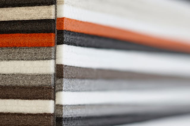 Stapel stoffen stalen in verschillende kleuren: donkerbruin, beige, oranje en grijs, weergegeven als meubelstofmonsterset.