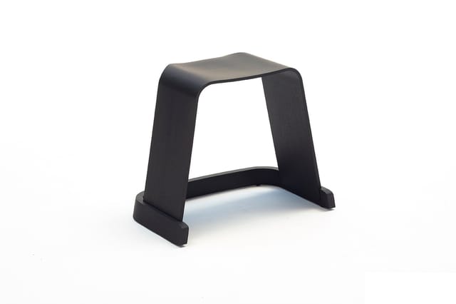Zwart houten kruk met gebogen zijkanten en voetsteun, minimalistische vorm tegen witte achtergrond.