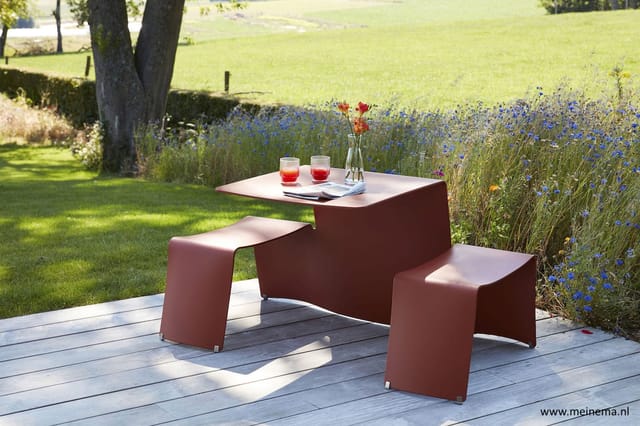 Rood-bruine picknicktafel met bijbehorende banken op houten terras, uitzicht op bloemenweide en grasveld.