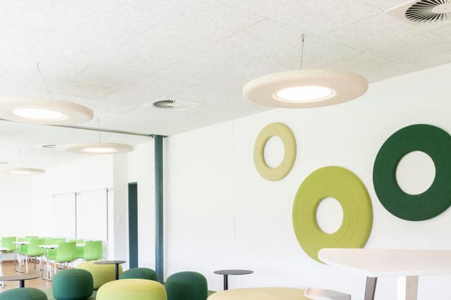 Modern kantoor met witte wanden, groene en gele stoelen, ronde wanddecoraties in groen en geel, inbouwverlichting en groene k