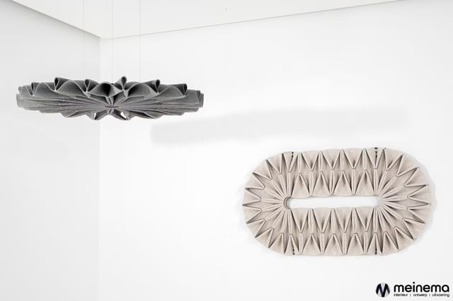 Twee hangende akoestische panelen: één donkergrijs lineair ontwerp bovenaan, één beige ovaal ontwerp onderaan met golfvormige
