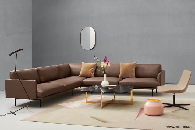 Bruine hoekbank met gouden kussens, zwarte marmeren salontafel met houten onderstel, beige fauteuil, staanlamp, roze poef en