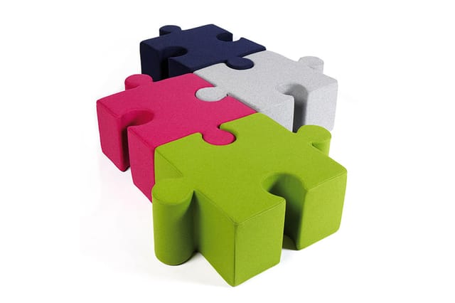 Puzzle vormige modulaire zitblokken in groen, roze, grijs en donkerblauw met ineinander grijpende vormen.