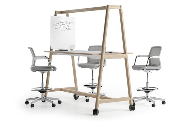 Houten vergadertafel met whiteboard, drie grijze bureaustoelen met wielen en voetsteun, kantoorruimte-opstelling.