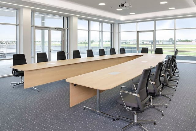 Moderne vergaderruimte met twee lichte houten vergadertafels, zwarte bureaukstoelen, grote raampartijen met uitzicht op lands