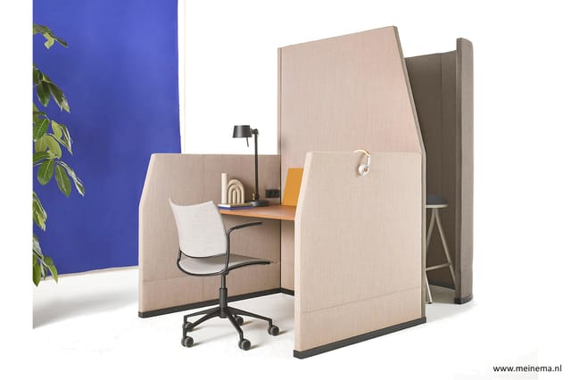 Akoestische belcel in beige stof met geïntegreerd bureau, witte stoel en zwart bureaulampje tegen blauwe wand.
