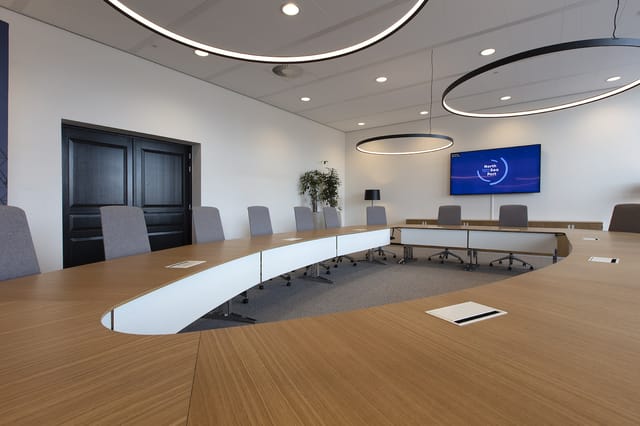 Moderne vergaderruimte met nierenvorming witte vergadertafel, grijze bureaustoelen, houten vloer, circulaire hanglamp, displa