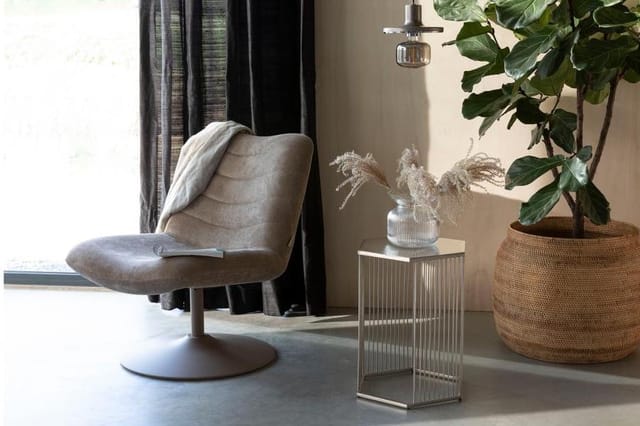 Grijze draaibare fauteuil met voetsteun naast glazen bijzettafel en wicker plantenbak in moderne kantoorruimte.
